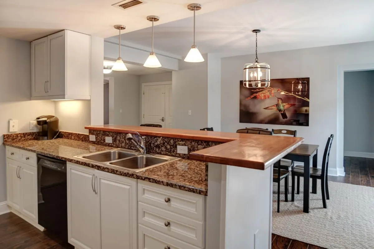 An inviting view that captures the kitchen countertop extending into the adjacent dining area, with modern lighting and wall art in view. The image highlights the open connection between the kitchen and social spaces, creating a seamless flow for gatherings or family meals.
