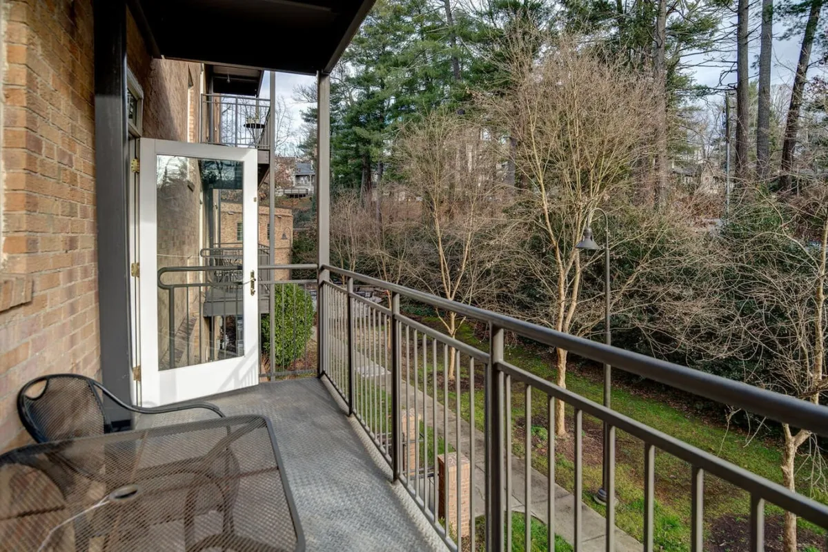 An inviting condo balcony with a seating area and views of leafy trees. The calm setting suggests the perfect spot for morning coffee or a glass of wine after exploring the village.