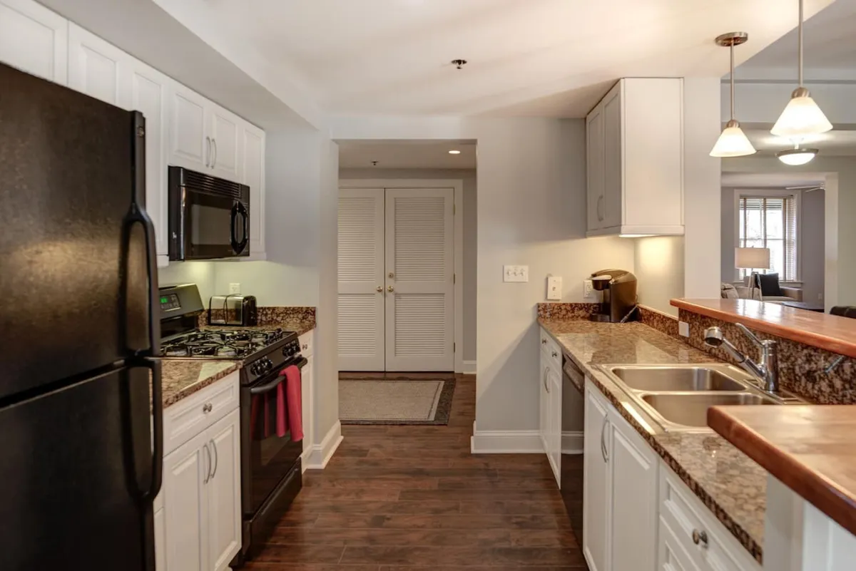 A welcoming kitchen scene featuring a black refrigerator, granite countertops, a dual sink, and a central kitchen island. The space is clearly designed for cooking and entertaining, with plenty of room for meal prep or socializing with guests while working in the kitchen.