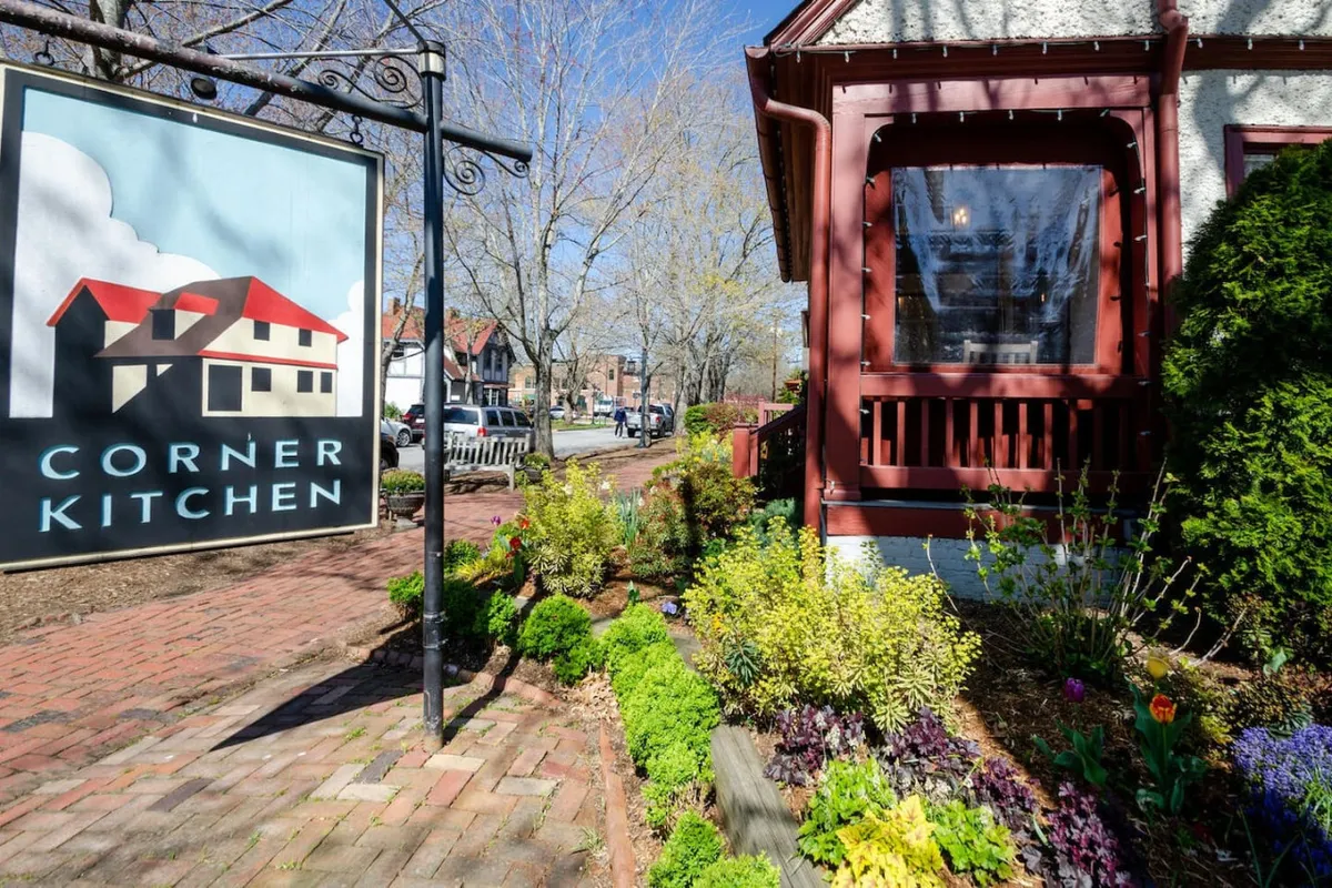 This exterior image features the inviting signage of the Corner Kitchen, a local landmark restaurant, with a carefully landscaped garden and the charming facade of the historic building. The sidewalk and greenery set a romantic and welcoming tone, emphasizing the appeal of dining just steps from the condo.