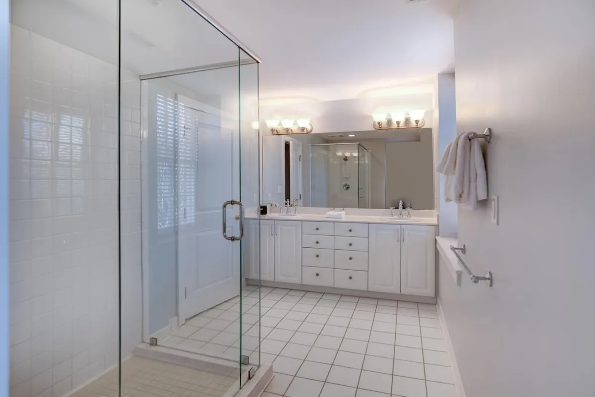 A modern, spa-inspired bathroom featuring a glass shower enclosure, double vanity, and mirrored cabinets, with sunlight streaming in to create a refreshing, calm ambiance.