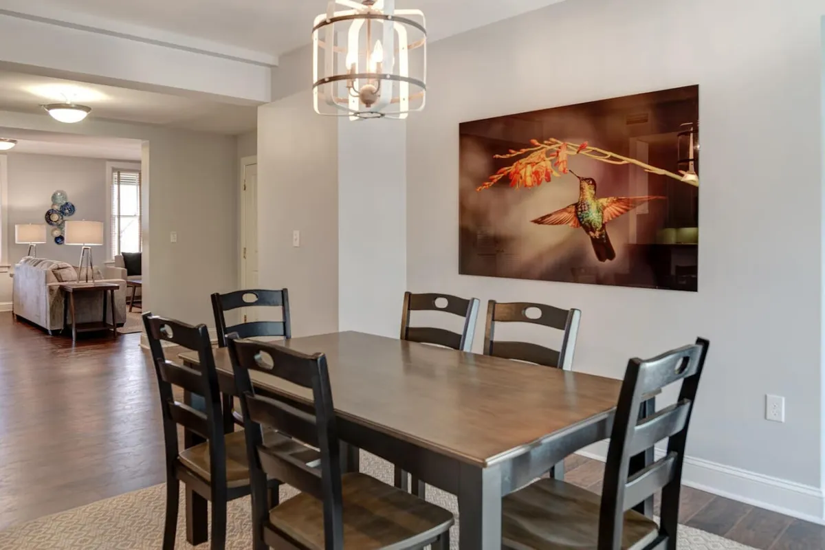 A warmly lit dining area centered around a large table, with a prominent hummingbird artwork and stylish lighting. The setting evokes memorable group dinners, celebrations, and social gatherings.