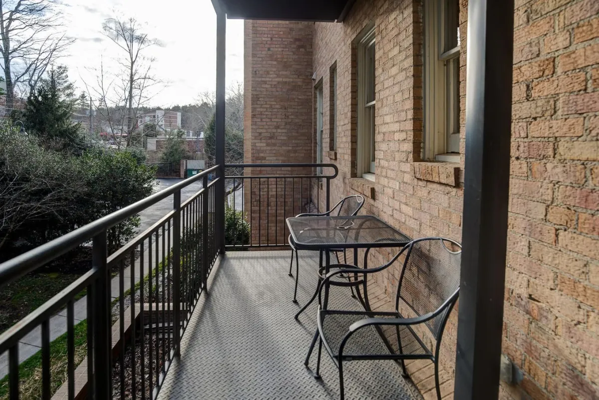 A serene balcony with a glass table, metal chairs, and views over lush surrounding greenery. The space invites quiet relaxation and offers an outdoor retreat just steps from your condo.