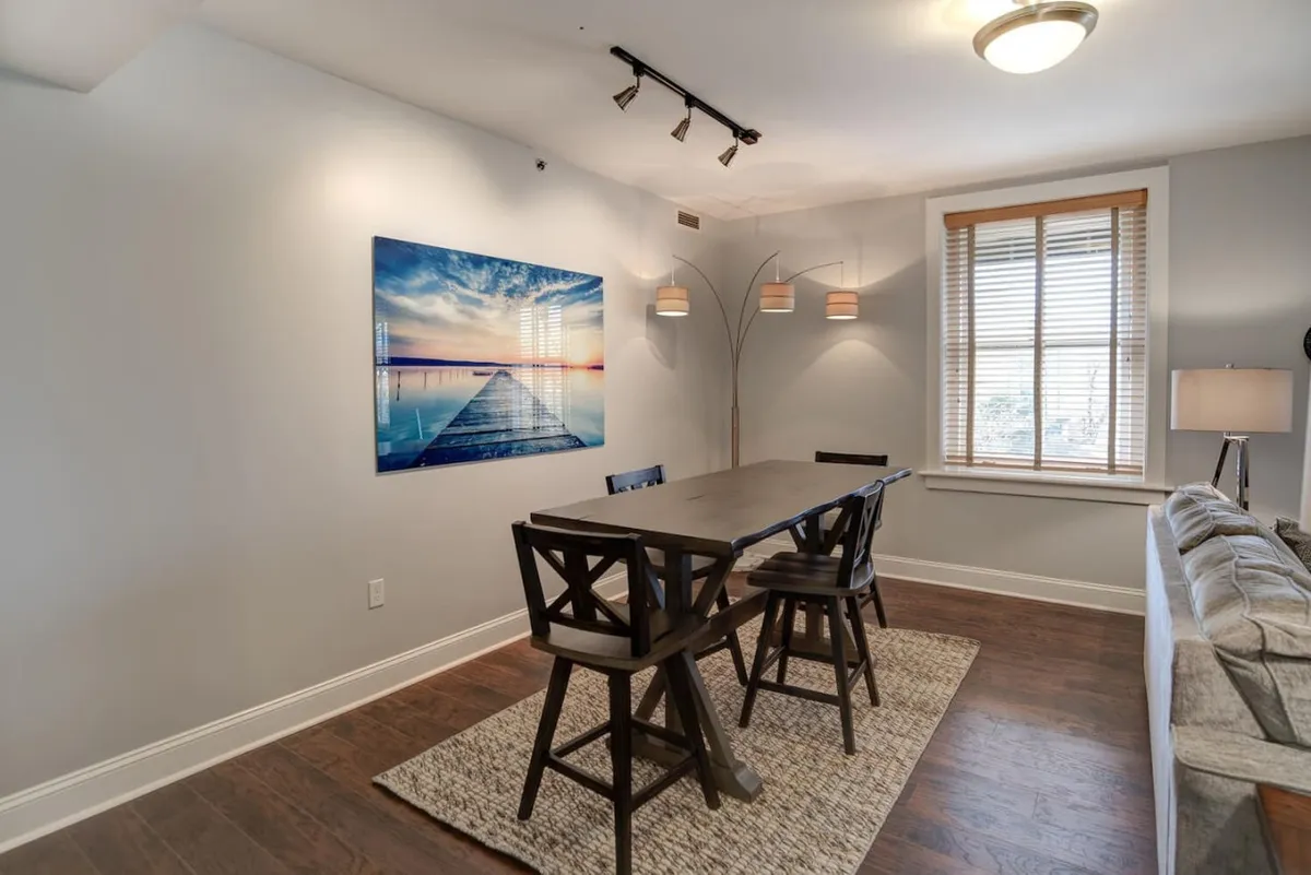A more intimate view of the dining table, complemented by tasteful artwork and a decorative floor lamp. The arrangement invites socializing, creative conversations, or cozy dinners, all set against a backdrop of curated décor and warm lighting.